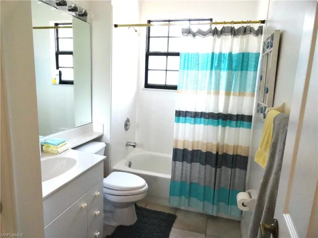 Full bathroom with vanity, shower / bathtub combination with curtain, toilet, and tile patterned floors