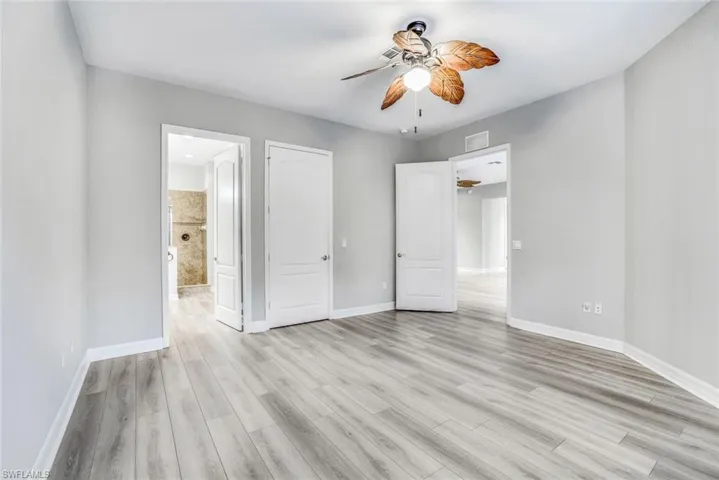 Unfurnished bedroom featuring ceiling fan, light wood finished floors, and ensuite bath