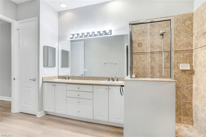 Bathroom featuring double vanity, a walk in shower, and light wood-style flooring