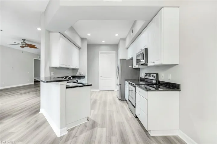 Kitchen featuring appliances with stainless steel finishes, white cabinets, dark stone countertops, light wood-style floors, and a ceiling fan