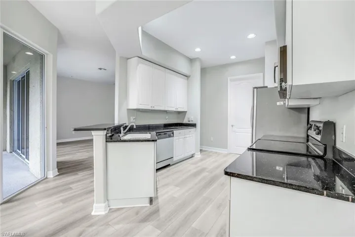Kitchen featuring white cabinets, dark stone countertops, light wood-style floors, appliances with stainless steel finishes, and recessed lighting