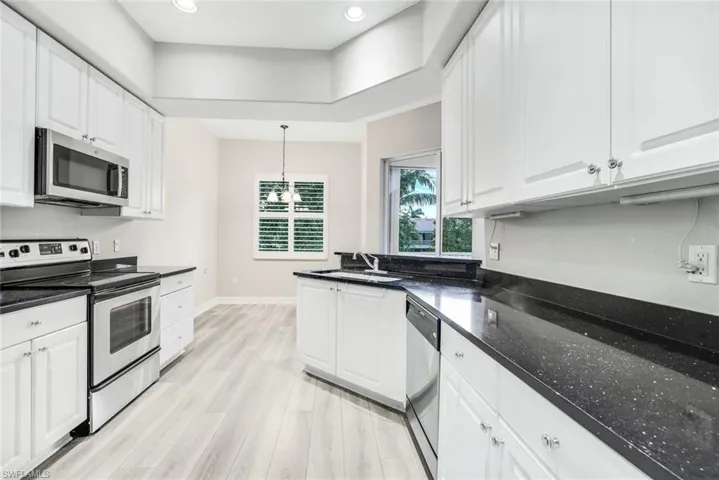 Kitchen featuring appliances with stainless steel finishes, white cabinets, light wood finished floors, pendant lighting, and dark stone counters