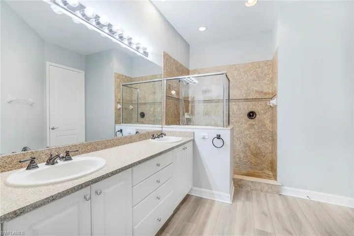 Bathroom with double vanity, a walk in shower, and light wood-type flooring