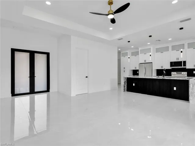 Dual tone kitchen with glass fronted cabinets, a ceiling fan, stainless steel appliances, a raised ceiling, and a large island with sink