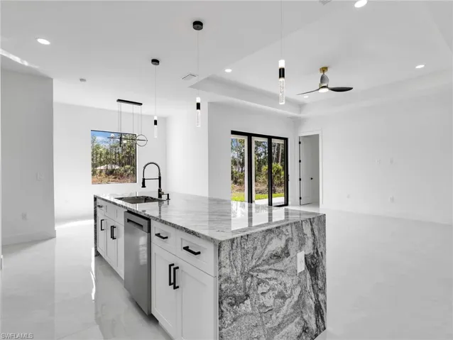 Kitchen featuring a center island with sink, light stone countertops, white cabinetry, a tray ceiling, and stainless steel dishwasher
