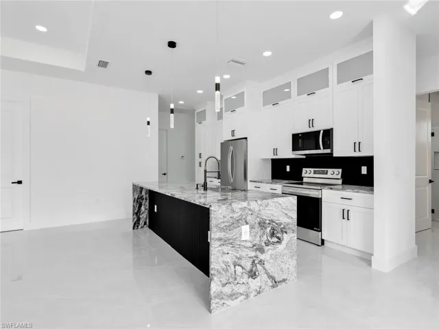 Kitchen with light stone counters, stainless steel appliances, white cabinetry, and glass fronted cabinets