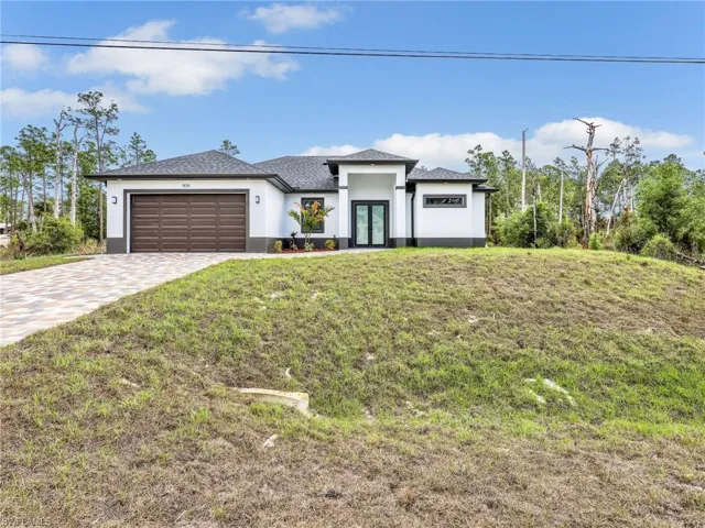 Prairie-style home with a front yard, an attached garage, decorative driveway, stucco siding, and a shingled roof