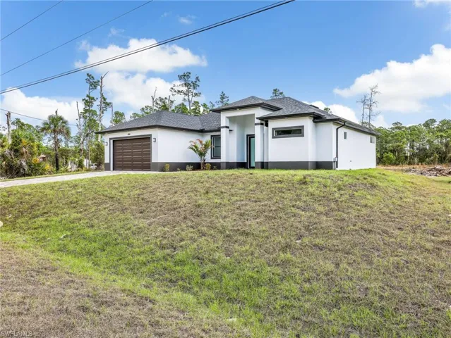 Prairie-style house featuring a front lawn, stucco siding, an attached garage, and driveway