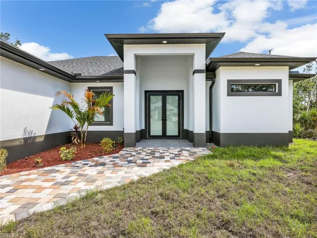 View of exterior entry with french doors, stucco siding, a lawn, and roof with shingles