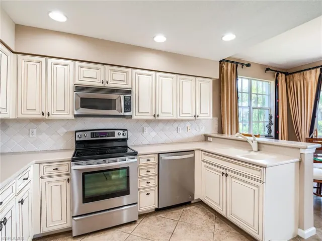 Kitchen with sink, decorative backsplash, light tile patterned floors, stainless steel appliances, and kitchen peninsula