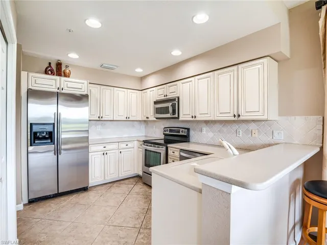 Kitchen with appliances with stainless steel finishes, decorative backsplash, kitchen peninsula, light tile patterned flooring, and a breakfast bar