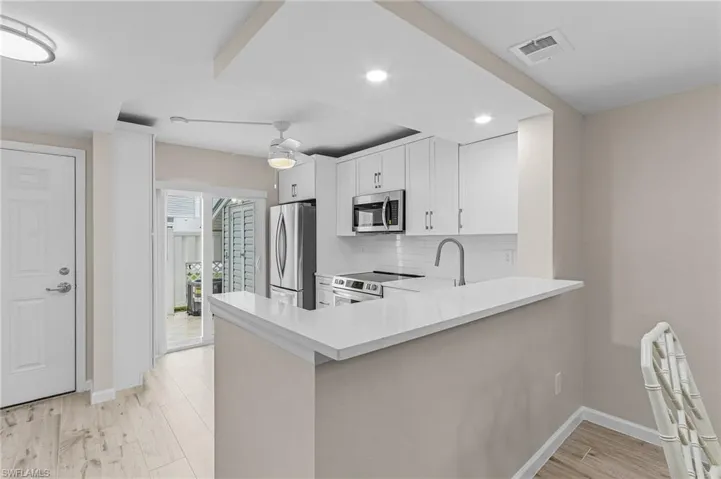 Kitchen featuring light hardwood / wood-style floors, appliances with stainless steel finishes, tasteful backsplash, and kitchen peninsula