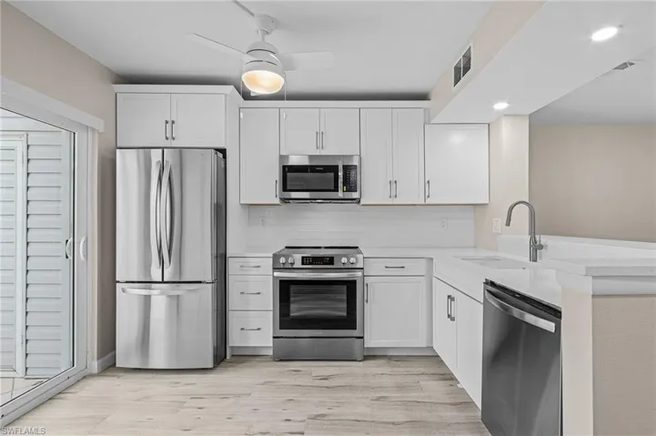 Kitchen with sink, light hardwood / wood-style floors, ceiling fan, stainless steel appliances, and white cabinets