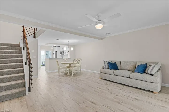 Living room featuring light hardwood / wood-style floors, ceiling fan with notable chandelier, and crown molding