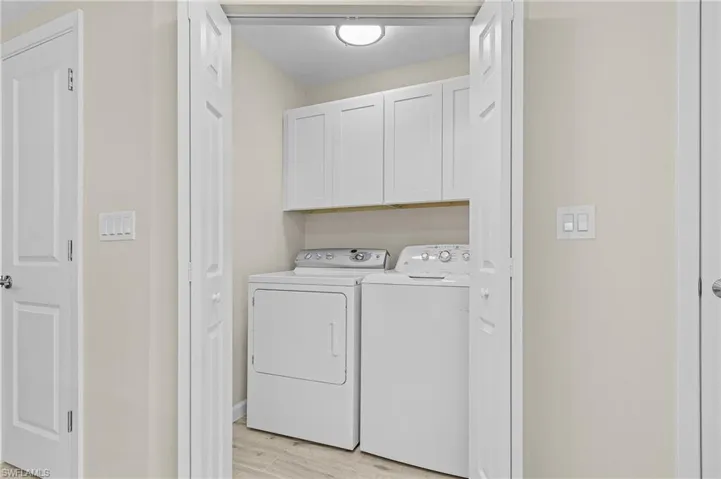 Washroom featuring light hardwood / wood-style floors, separate washer and dryer, and cabinets