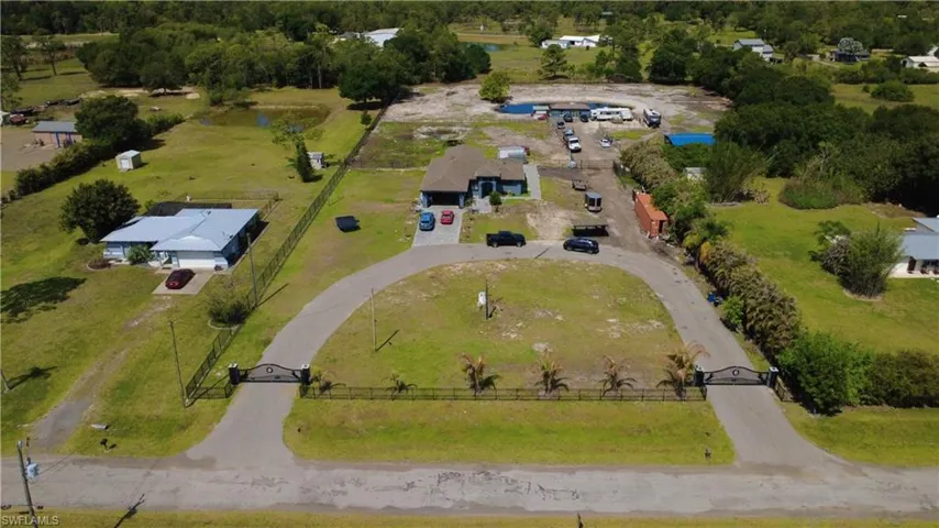 Gated property entrance with a paved circular driveway, expansive green lawn, and mature trees