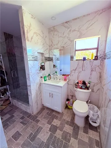 Bathroom featuring marble-look wall tiling, a white vanity with an integrated sink, a glass-enclosed shower, and multi-toned rectangular floor tiles