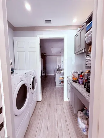 Dedicated laundry area featuring a stacked washer and dryer, wood-finish flooring, recessed lighting, and a utility counter with storage cabinetry