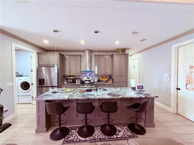 Kitchen featuring an oversized island with seating, pendant lighting, stainless steel appliances, grey cabinetry, and wood-finish flooring
