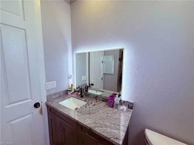 Vanity featuring a built-in sink, stone countertop, dark wood-finish cabinetry, and an illuminated mirror