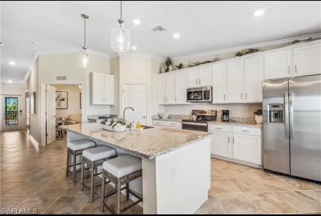 Kitchen with appliances with stainless steel finishes, crown molding, white cabinets, a breakfast bar area, and hanging light fixtures