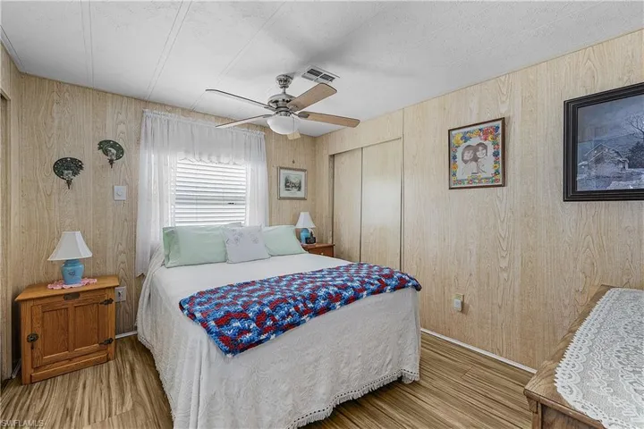 Bedroom with visible vents, a closet, ceiling fan, wooden walls, and wood finished floors