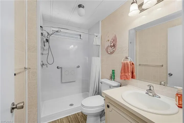 Bathroom featuring toilet, a stall shower, vanity, and tile walls