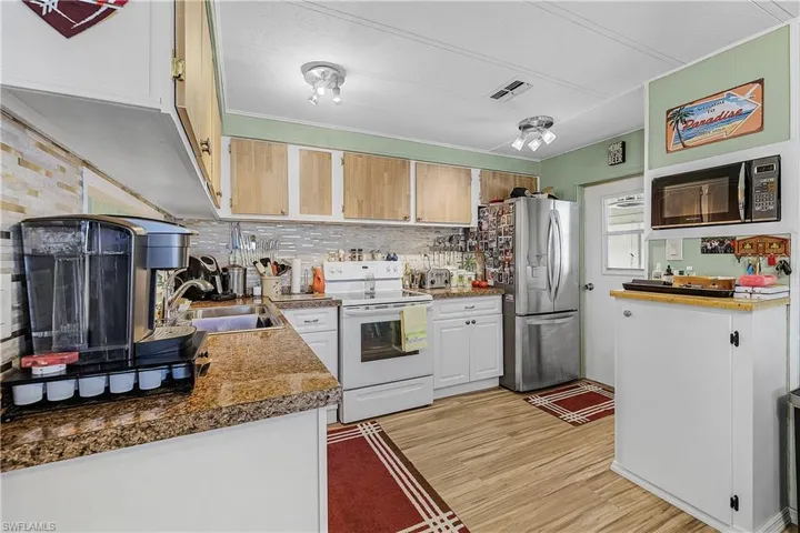 Kitchen with visible vents, stainless steel refrigerator with ice dispenser, a sink, light wood-style floors, and white electric range oven