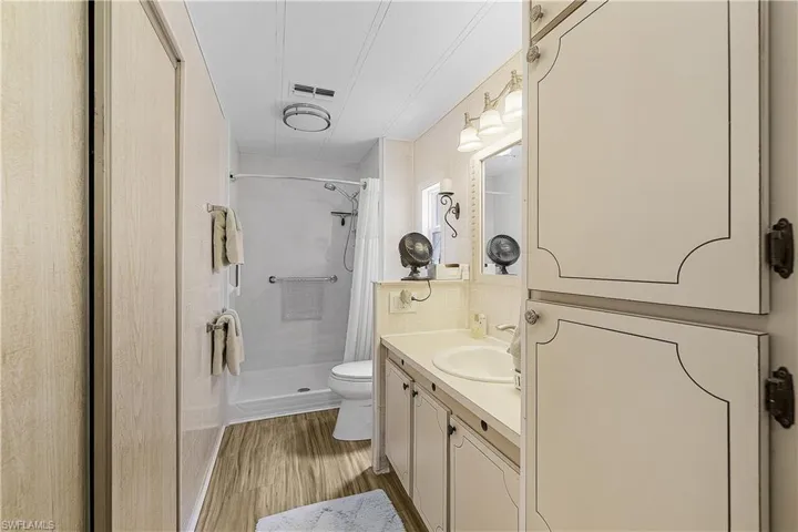 Bathroom with vanity, toilet, a shower stall, visible vents, and wood finished floors
