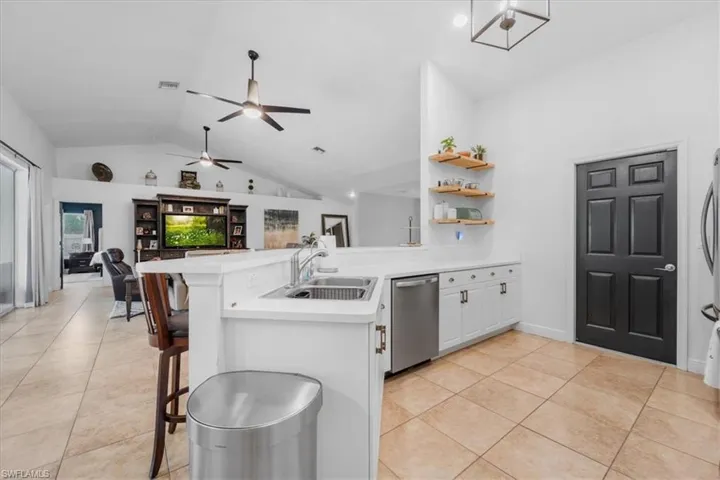 Kitchen with vaulted ceiling, a sink, dishwasher, light countertops, and a peninsula