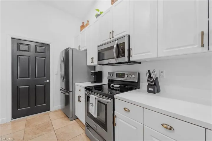 Kitchen featuring white cabinets, light tile patterned flooring, baseboards, light countertops, and appliances with stainless steel finishes