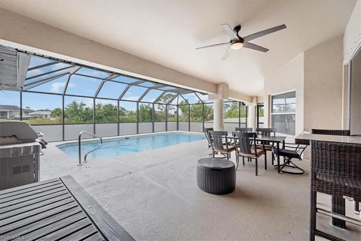 Pool with glass enclosure, grilling area, a ceiling fan, and a patio