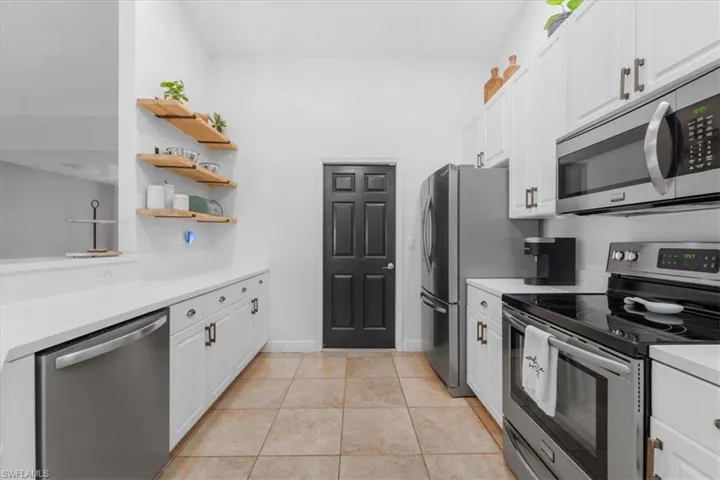 Kitchen with open shelves, light tile patterned floors, white cabinetry, light countertops, and appliances with stainless steel finishes