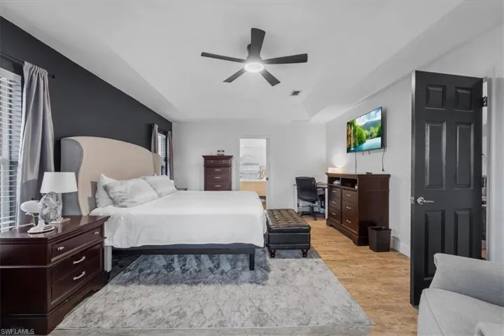 Bedroom featuring a tray ceiling, visible vents, baseboards, light wood-style flooring, and ceiling fan