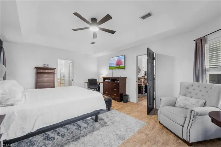 Bedroom featuring light wood finished floors, a raised ceiling, visible vents, ensuite bath, and ceiling fan