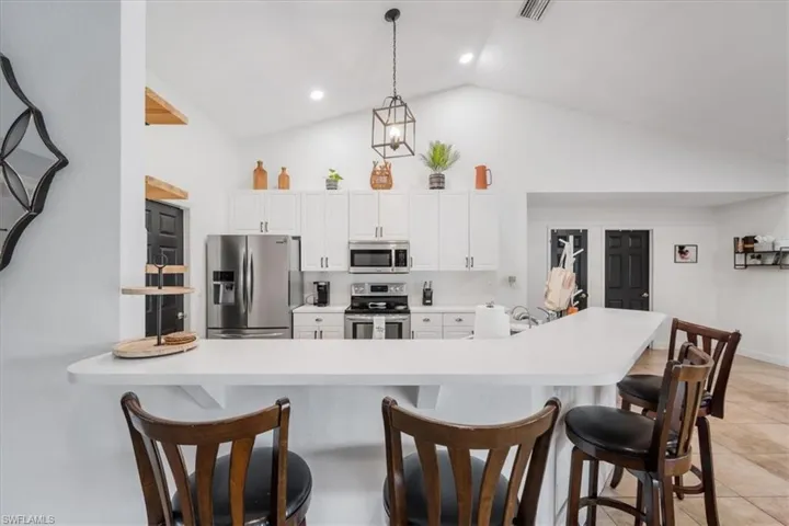 Kitchen with a kitchen bar, high vaulted ceiling, stainless steel appliances, and light countertops