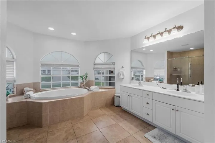 Bathroom with a sink, a stall shower, a bath, double vanity, and tile patterned flooring