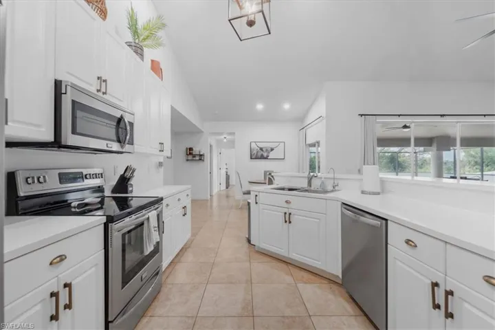 Kitchen featuring white cabinets, lofted ceiling, light tile patterned floors, a sink, and appliances with stainless steel finishes
