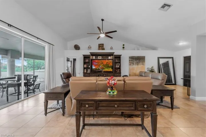Living room with lofted ceiling, a ceiling fan, visible vents, and light tile patterned flooring