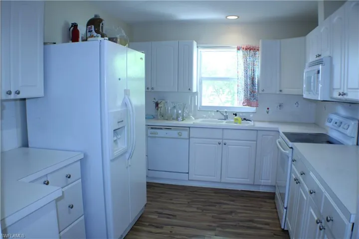 Kitchen featuring dark hardwood / wood-style floors, white appliances, tasteful backsplash, sink, and white cabinetry