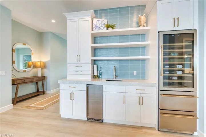 Indoor wet bar featuring open shelves, wine cooler, white cabinetry, light stone countertops, and backsplash