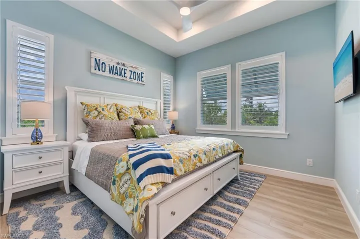 Bedroom with light wood finished floors, multiple windows, a raised ceiling, and a ceiling fan