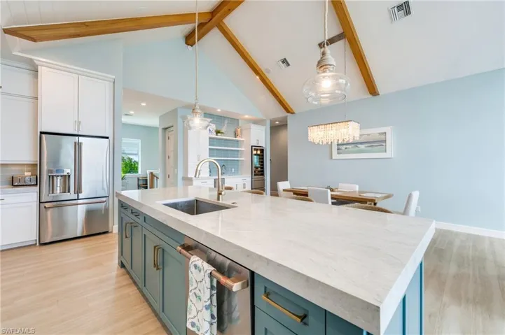 Two tone kitchen featuring two tone cabinets, high end fridge, light wood-style flooring, light stone countertops, and a center island with sink