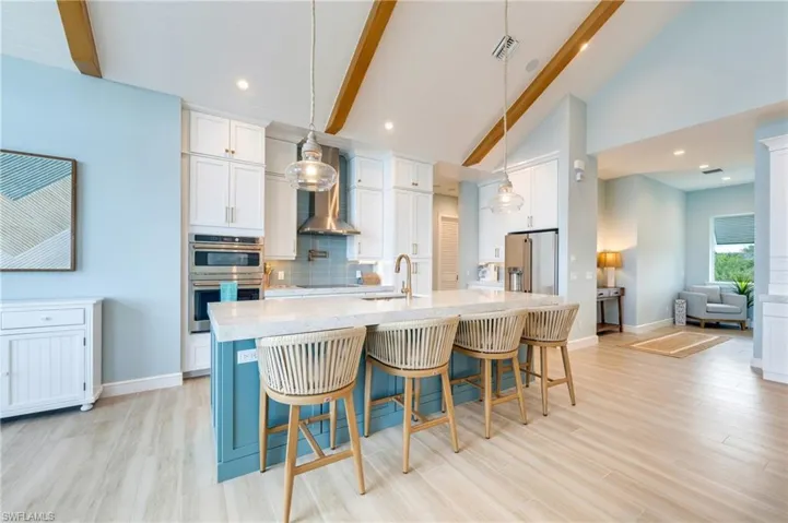 Kitchen with a kitchen breakfast bar, light stone counters, dual tone cabinetry, a kitchen island with sink, and light wood-style flooring