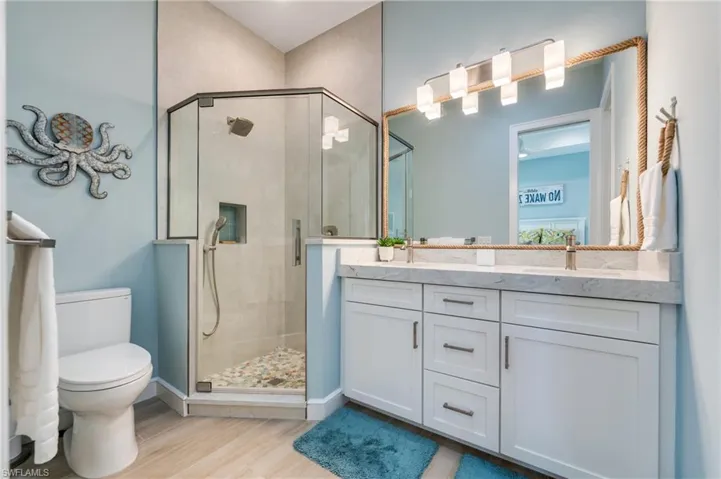 Full bath featuring double vanity, a shower stall, and light wood-style flooring