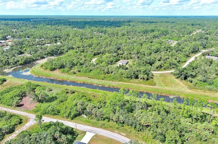 Aerial view of property and surrounding area featuring a forest and a nearby body of water