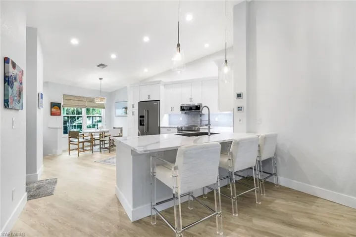 Kitchen with a breakfast bar, a sink, white cabinetry, appliances with stainless steel finishes, and pendant lighting