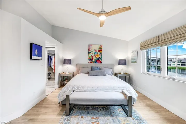 Bedroom with light wood finished floors, a spacious closet, vaulted ceiling, ceiling fan, and baseboards