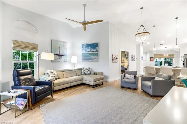 Living room with baseboards, light wood-style flooring, a high ceiling, and ceiling fan with notable chandelier