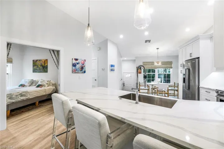 Kitchen featuring white cabinets, high quality fridge, light stone countertops, pendant lighting, and a sink
